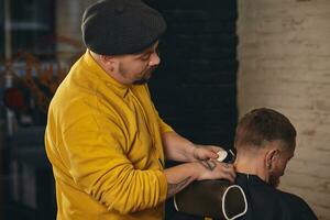 Barber making haircut of attractive bearded man in barbershop photo