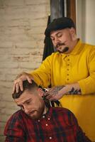 Barber making haircut of attractive bearded man in barbershop photo