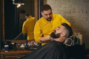 Client with big black beard during beard shaving in barber shop photo