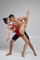 The couple of an athletic modern ballet dancers are posing against a gray studio background. photo