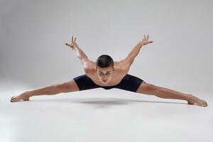 Photo of a handsome man ballet dancer, dressed in a black shorts, making a dance element against a gray background in studio.