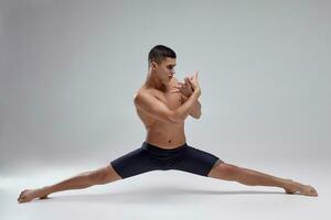 foto de un hermoso hombre ballet bailarín, vestido en un negro bermudas, haciendo un danza elemento en contra un gris antecedentes en estudio.