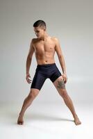 Photo of a handsome man ballet dancer, dressed in a black shorts, making a dance element against a gray background in studio.