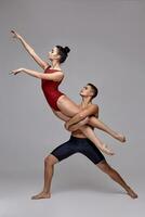 The couple of an athletic modern ballet dancers are posing against a gray studio background. photo