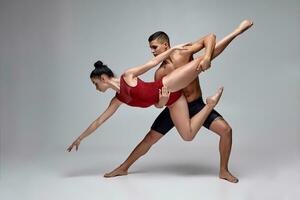 The couple of an athletic modern ballet dancers are posing against a gray studio background. photo