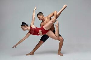 The couple of an athletic modern ballet dancers are posing against a gray studio background. photo