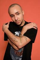 Studio shot of a young tattoed bald man posing against a pink background. 90s style. photo