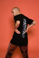 Studio shot of a young tattoed bald man posing against a pink background. 90s style. photo