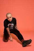 Studio shot of a young tattoed bald man posing against a pink background. 90s style. photo