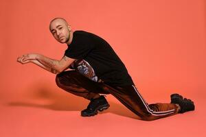 Studio shot of a young tattoed bald man posing against a pink background. 90s style. photo