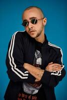 Studio shot of a young tattoed bald man posing against a blue background. 90s style. photo