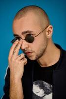 Studio shot of a young tattoed bald man posing against a blue background. 90s style. photo