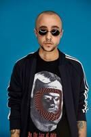 Studio shot of a young tattoed bald man posing against a blue background. 90s style. photo