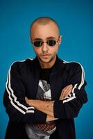 Studio shot of a young tattoed bald man posing against a blue background. 90s style. photo