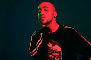 Studio shot of a young tattoed bald man posing against a colorful background. 90s style. photo