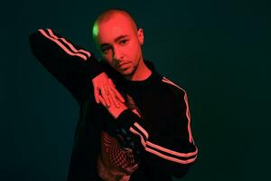 Studio shot of a young tattoed bald man posing against a colorful background. 90s style. photo