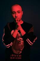 Studio shot of a young tattoed bald man posing against a dark blue background. 90s style. photo