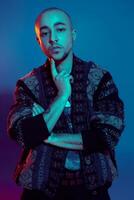 Studio shot of a young tattoed bald man posing against a colorful background. 90s style. photo