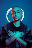 Studio shot of a young tattoed bald man posing against a blue background. 90s style. photo