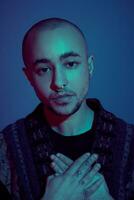 Studio shot of a young tattoed bald man posing against a blue background. 90s style. photo