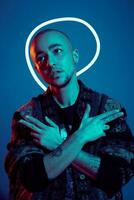 Studio shot of a young tattoed bald man posing against a blue background. 90s style. photo