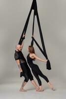 Beautiful girl and an athletic man in a black sport suits are performing an acrobatic elements in a studio. photo