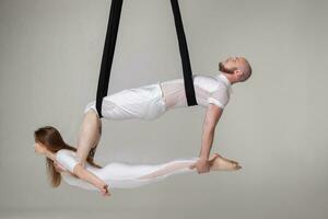 Beautiful girl and an athletic man in a white sport suits are performing an acrobatic elements in a studio. photo