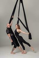 Beautiful girl and an athletic man in a black sport suits are performing an acrobatic elements in a studio. photo