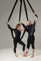 Beautiful girl and an athletic man in a black sport suits are performing an acrobatic elements in a studio. photo