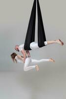 Beautiful girl and an athletic man in a white sport suits are performing an acrobatic elements in a studio. photo