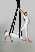 Beautiful girl and an athletic man in a white sport suits are performing an acrobatic elements in a studio. photo