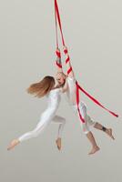 Beautiful girl and an athletic man in a white sport suits are performing an acrobatic elements in a studio. photo