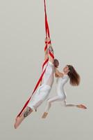 hermosa niña y un atlético hombre en un blanco deporte trajes son ejecutando un acrobático elementos en un estudio. foto