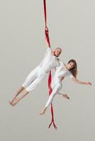 Beautiful girl and an athletic man in a white sport suits are performing an acrobatic elements in a studio. photo