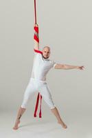 Athletic man in a white sport suit is performing an acrobatic elements in a studio. photo