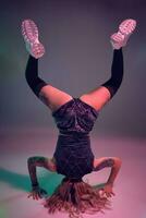 young beautiful blonde gymnast girl in velour blue booty shorts and black stockings standing upside down on pink background photo