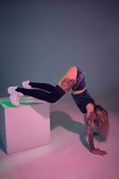 young beautiful blonde gymnast girl in velour blue booty shorts and black stockings standing upside down on pink background photo