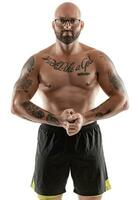 atlético calvo, tatuado hombre en negro pantalones cortos es posando aislado en blanco antecedentes. de cerca retrato. foto