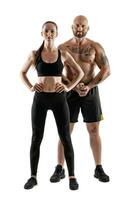 Athletic man in black shorts and sneakers with brunette woman in leggings and top posing isolated on white background. Fitness couple, gym concept. photo