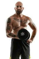 Athletic bald, tattooed man in black shorts is posing with a dumbbell isolated on white background. Close-up portrait. photo