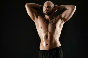 Athletic bald, bearded, tattooed man in black shorts is posing against a black background. Close-up portrait. photo