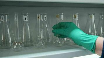 multiple laboratory flasks on the shelf ready to be used. Clip. Hand of a doctor or scientist in glove taking one empty glass flask. video
