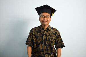 Expressive of Adult indonesia male wear batik, toga cup or graduation hat and eyeglasses isolated on white background, expressions of portrait graduation photo