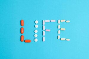 Life word from Colorful Medicine Pills isolated on blue background, supplement, vitamin, colorful photo