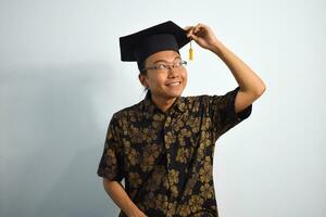 Expressive of Adult indonesia male wear batik, toga cup or graduation hat and eyeglasses isolated on white background, expressions of portrait graduation photo