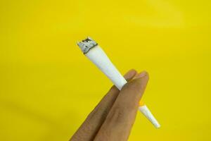 un hombre mano sostiene un hecho a mano cigarrillo en amarillo antecedentes foto