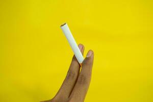 A man hand holds a handmade cigarette on yellow background photo