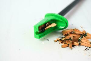 green pencil sharpener and dark green pencils, pencil shavings on white background photo