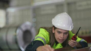 ingénieur femme permanent avec confiance avec vert travail suite robe et sécurité casque dans de face de entrepôt de acier rôle matériel. intelligent industrie ouvrier en fonctionnement. video