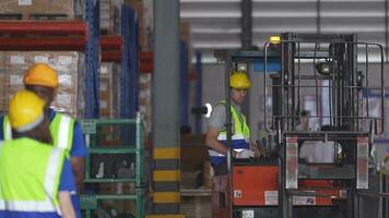 factory man driving forklift car working in distribution warehouse. factory worker teammates working beside stacks of cargo. Group of Diversity engineer factory people meeting. video